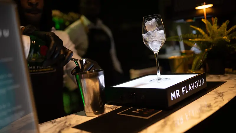 Mixologist pouring a signature cocktail at a marble bar with a Mr Flavour lightbox