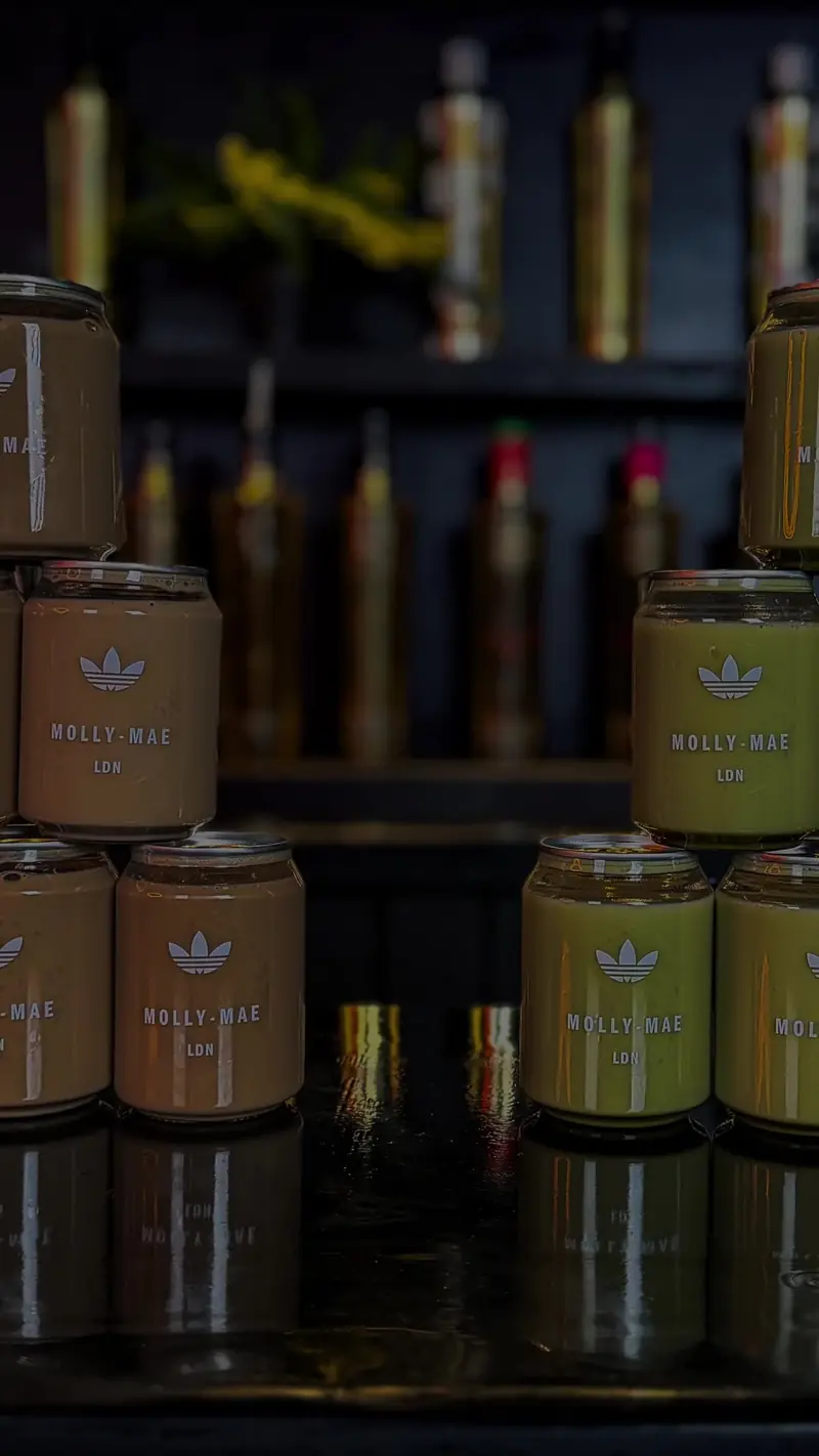 Branded iced matcha and iced latte cans for the Adidas x Molly-Mae launch, stacked with Adidas trefoil and Molly-Mae LDN label artwork