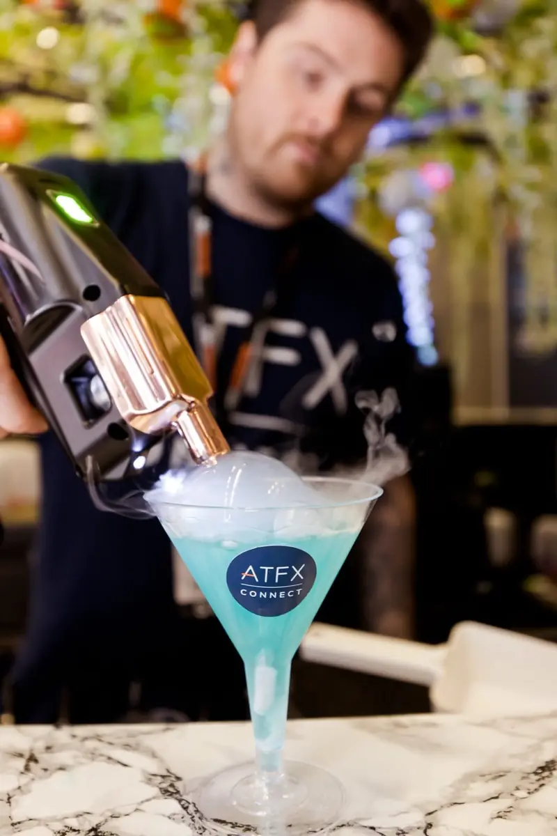 A Mr Flavour mixologist torch-finishing a branded ATFX dry ice cocktail at the Finance Magnates London Summit