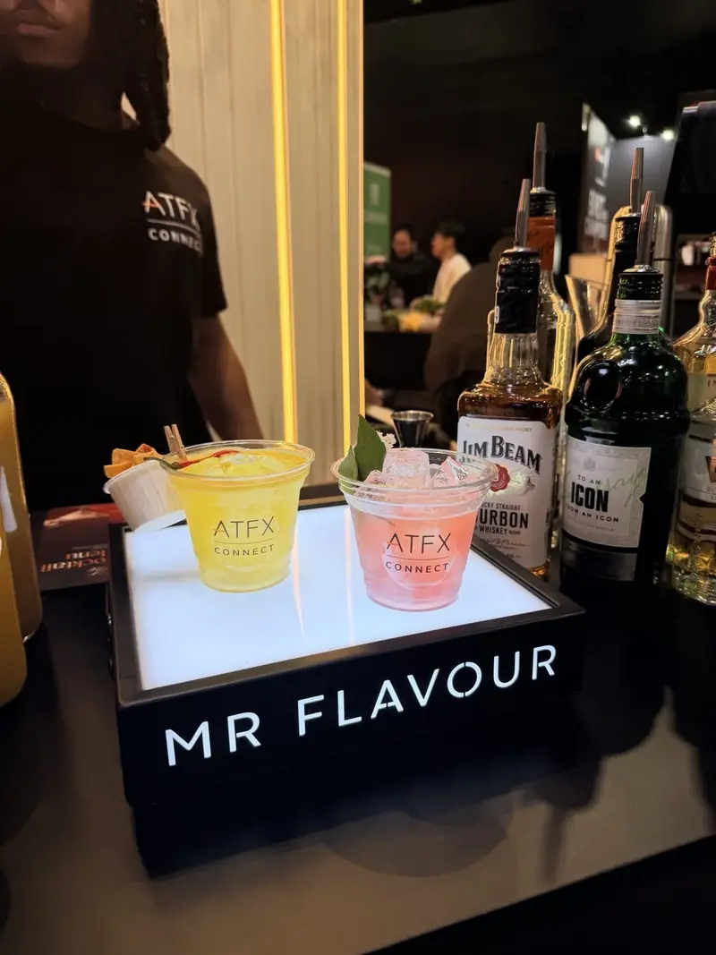 A Mr Flavour bartender behind the illuminated Mr Flavour counter with branded ATFX serves at the Finance Magnates London Summit