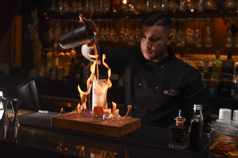 Mr Flavour bartender pouring a flaming serve over a burning cocktail at a dark bar